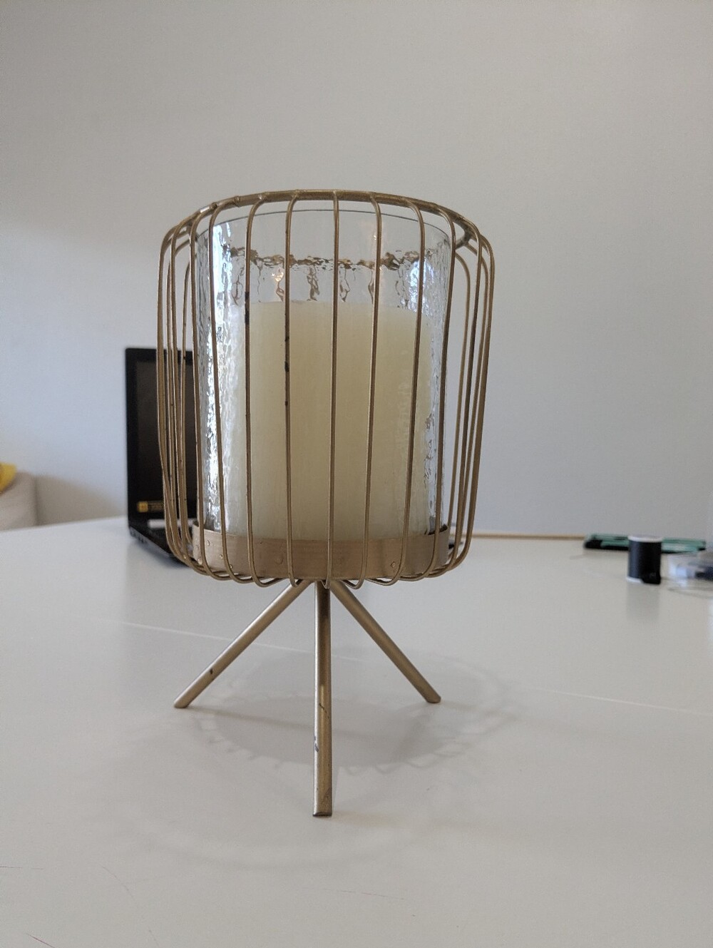 Gold-tone metal wire-cage hurricane candle holder on a three-legged tripod stand